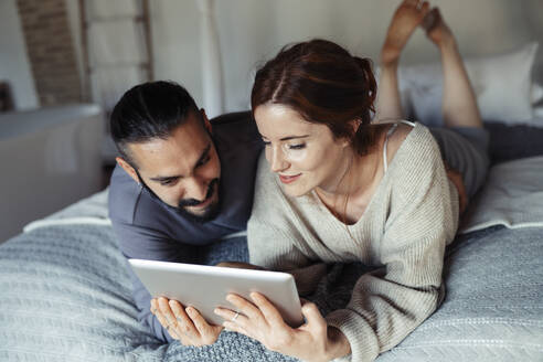 Mann und Frau benutzen ein digitales Tablet, während sie zu Hause auf dem Bett liegen - JSMF01843