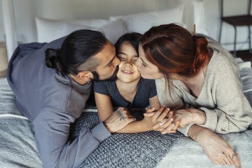Mutter und Vater küssen ihre Tochter, während sie zu Hause auf dem Bett liegen - JSMF01846