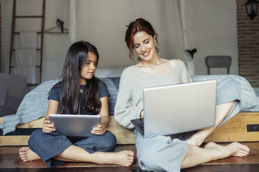 Mutter zeigt ihrer Tochter den Laptop, während sie zu Hause sitzt - JSMF01851