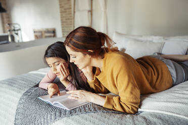 Mutter und Tochter lesen ein Buch, während sie zu Hause auf dem Bett liegen - JSMF01856