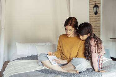 Mutter unterrichtet Tochter, während sie zu Hause auf dem Bett sitzt - JSMF01858