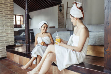 Lächelnde Frau und Mädchen in Handtuch mit Obst und Saft beim Sitzen zu Hause - JSMF01861