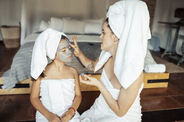 Frau beim Auftragen von Gesichtscreme auf das Gesicht ihrer Tochter, während sie zu Hause sitzt - JSMF01871