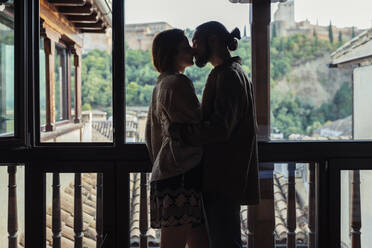 Couple kissing while standing by window at home - JSMF01887