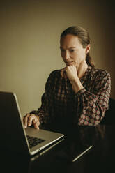 Geschäftsfrau, die im Büro sitzend am Laptop arbeitet - DMGF00181