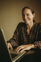 Smiling businesswoman working on laptop while sitting in office - DMGF00187