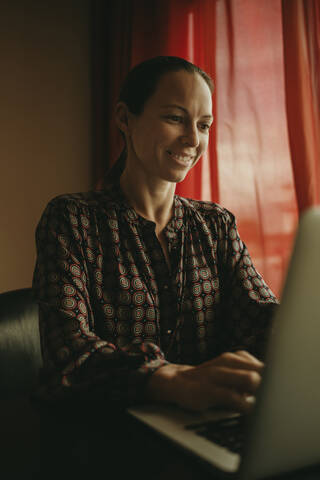 Geschäftsfrau lächelnd bei der Arbeit am Laptop im Büro, lizenzfreies Stockfoto