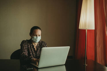 Geschäftsfrau mit Gesichtsschutzmaske bei der Arbeit am Laptop im Büro - DMGF00192