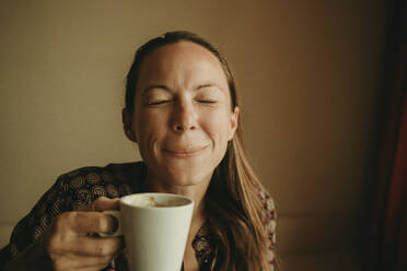 Female entrepreneur drinking coffee while sitting in office against wall - DMGF00200