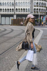 Lächelnde junge Frau mit Einkaufstaschen beim Überqueren von Bahngleisen - BOYF01620