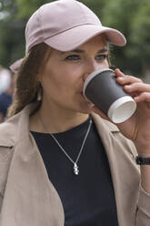 Beautiful young woman looking away while drinking coffee standing on street - BOYF01623