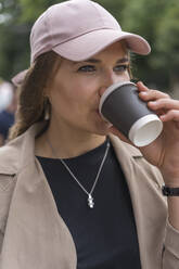 Schöne junge Frau schaut weg, während sie auf der Straße stehend Kaffee trinkt - BOYF01623