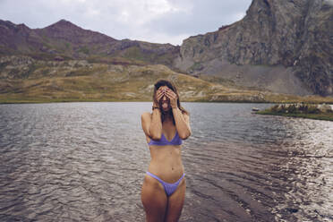 Frau im Bikini versteckt ihr Gesicht, während sie in einem See in Ibones of Anayet steht - RSGF00355