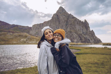 Sisters wearing warm clothing embracing while standing against lake at Ibones of Anayet - RSGF00356