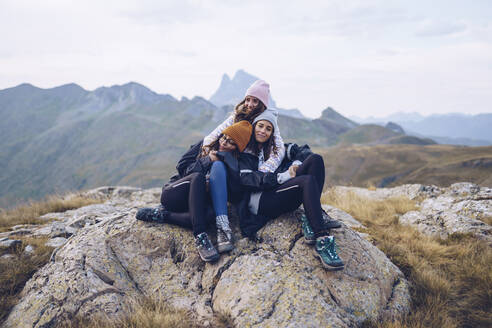Freunde, die sich umarmen, während sie auf einem Felsen um die Ibones von Anayet sitzen - RSGF00361