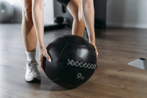 Close-up of woman lifting fitness ball while standing in gym - MPPF01147