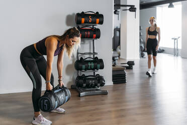 Weibliche Athletin, die einen Sandsack hebt, und eine andere Sportlerin, die im Fitnessstudio läuft - MPPF01156