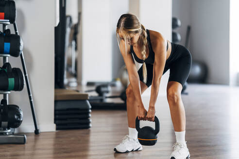 Young female athlete lifting Kettle bell standing in gym - MPPF01167