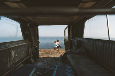 Paar bewundert die Aussicht, während es mit dem Arm am Strand steht - DAMF00545