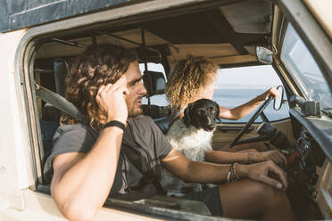 Junge Frau sitzt mit Hund und Mann beim Autofahren am Strand - DAMF00557