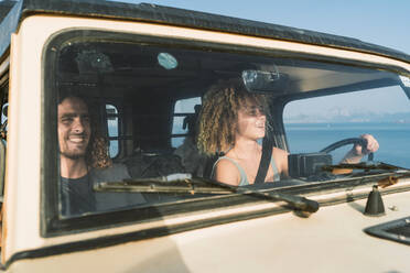 Lächelnde Frau am Steuer, während sie neben einem Mann im Auto am Strand sitzt - DAMF00558