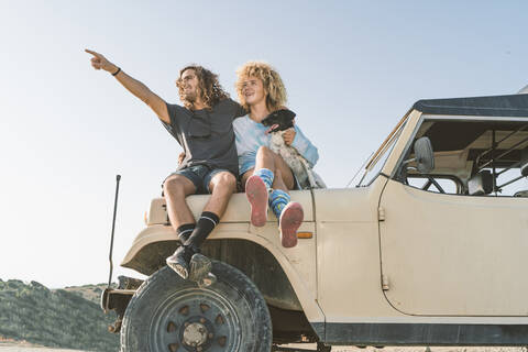 Man pointing while sitting by woman and dog on car at beach stock photo