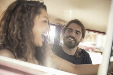 Fröhliche junge Frau am Steuer eines Autos mit einem männlichen Freund an einem sonnigen Tag - AJOF00217