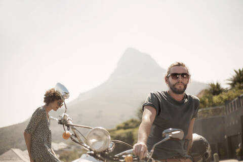 Mittlerer erwachsener Mann auf Motorrad sitzend mit Freundin an einem sonnigen Tag, lizenzfreies Stockfoto