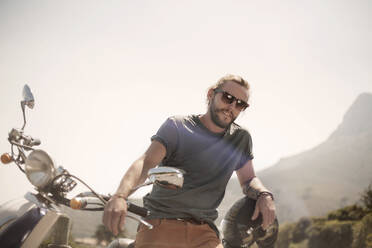 Mid adult man standing with motorcycle on sunny day - AJOF00227