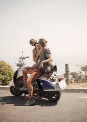 Male friends sitting on motorcycle during sunny day - AJOF00228