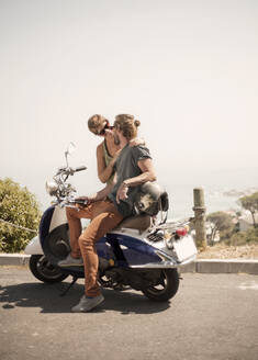 Männliche Freunde sitzen auf einem Motorrad an einem sonnigen Tag - AJOF00228