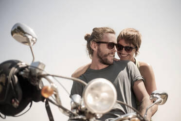 Smiling friends sitting on motorcycle during sunny day - AJOF00229