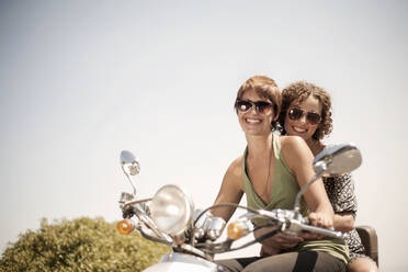 Female friends riding on motorcycle during sunny day - AJOF00230