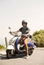 Mittlerer erwachsener Mann auf Motorrad sitzend an einem sonnigen Tag - AJOF00237