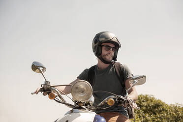 Mittlerer erwachsener Mann auf Motorrad sitzend und wegschauend an einem sonnigen Tag - AJOF00238