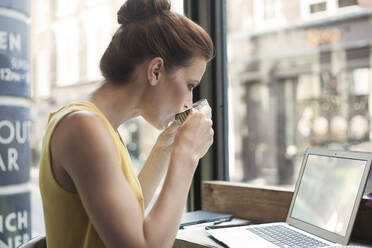 Young woman drinking coffee while using laptop in cafe - AJOF00256