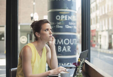 Nachdenkliche junge Geschäftsfrau mit Laptop in einem Café - AJOF00258