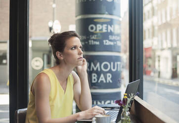 Thoughtful young businesswoman with laptop at coffee shop - AJOF00258