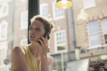 Junge Geschäftsfrau, die in einem Café mit einem Mobiltelefon spricht - AJOF00260