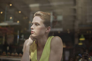 Thoughtful young businesswoman looking through window while sitting in cafe - AJOF00262