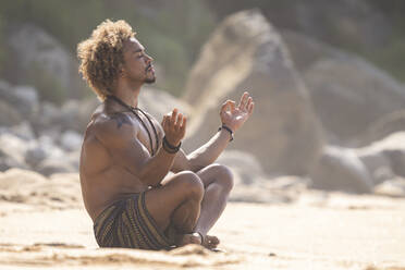 Hemdloser junger Mann gestikuliert beim Meditieren am Strand im Sommer - SNF00630