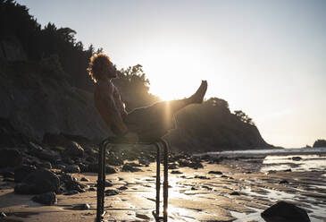 Young man exercising on parallel bars at beach against sky - SNF00656