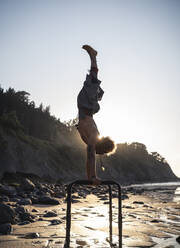 Junger Mann übt Handstand am Parallelbarren am Strand gegen den Himmel - SNF00657