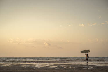 Junger Mann mit Surfbrett am Strand gegen den Himmel bei Sonnenuntergang - SNF00668