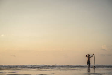 Mann stehend mit Surfbrett am Meer gegen den Himmel bei Sonnenuntergang - SNF00673