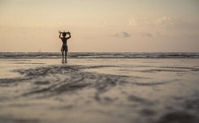 Man carrying surfboard on head while walking at seashore during sunset - SNF00675