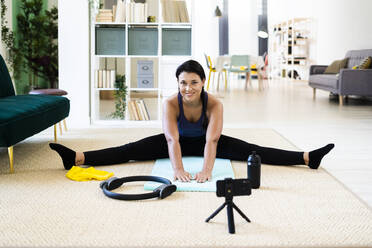 Female influencer video recording on camera while doing stretching exercise at home - GIOF09170