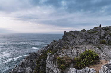 Man with fishing rod standing on Bufones de Pria cliffs at dusk, Asturias, Spain - JMPF00461