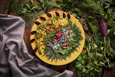 Draufsicht auf eine Komposition aus reifem Grün und Blütenblättern, die auf einem Holztisch angeordnet sind - ADSF16617