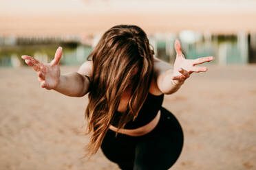 Unbekannte Frau steht in Anjaneyasana und streckt die Hände in Richtung Kamera, während sie am Strand Yoga macht - ADSF16670